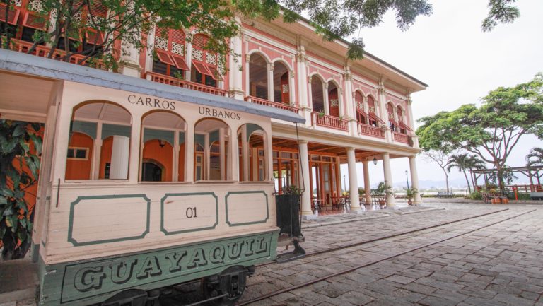 Trolley car in Guayaquil, Ecuador on cobblestone street by colonial pink building, seen on a Galapagos Travel Package tour.
