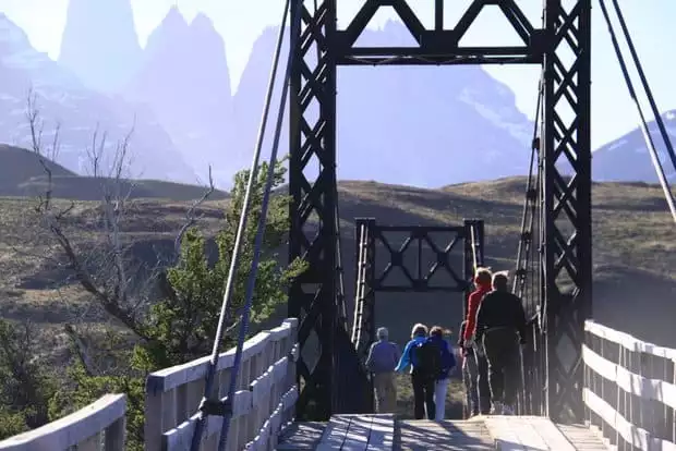 A group of tourist on a walking bridge with green hillsides and snowy mountains in Patagonia.
