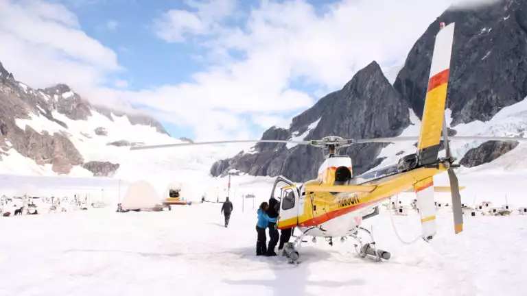 People getting out of a helicopter on top of a glacier next to a dog sledding camp in Alaska on a sunny day