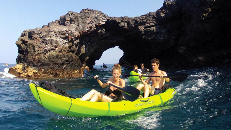 adventure travelers in neon kayaks in front of hawaiian lava tubes on a sunny day