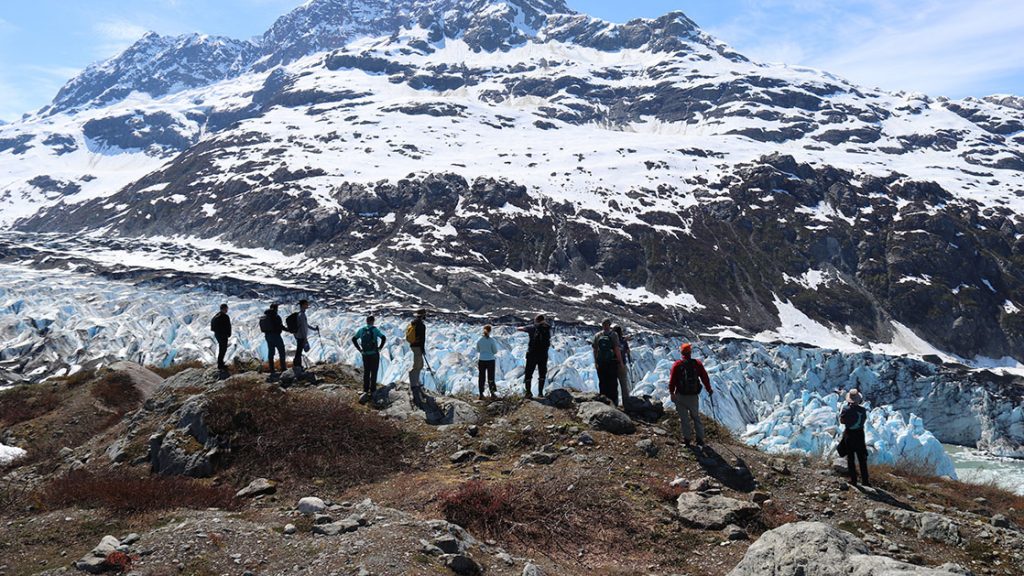 A group of travelers stands in front of a mountain and glacier in Alaska