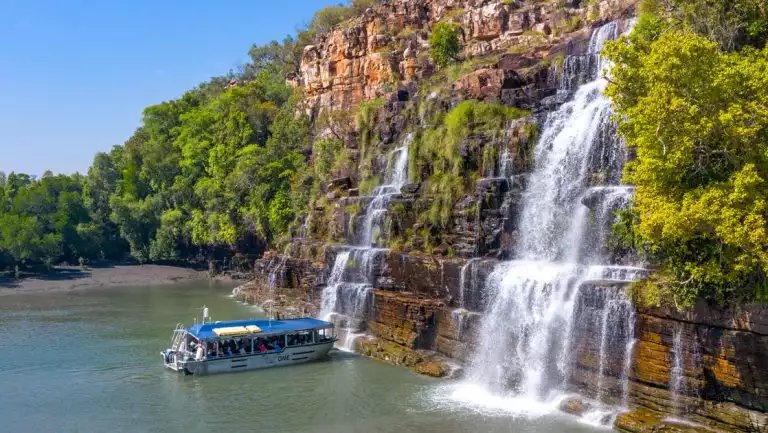 Silver Xplorer tender boat pulls up in front of cascading waterfalls under a blue sky in Australia's Kimberley Region.