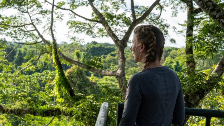 A girl stands at the rail overlooking the verdant green jungle while on the Ecuador Amazon Adventure with La Selva Ecolodge