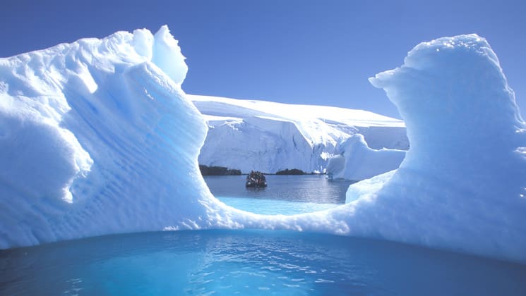 an illuminated antarctic iceberg in turquoise water on a sunny day with another larger iceberg behind it