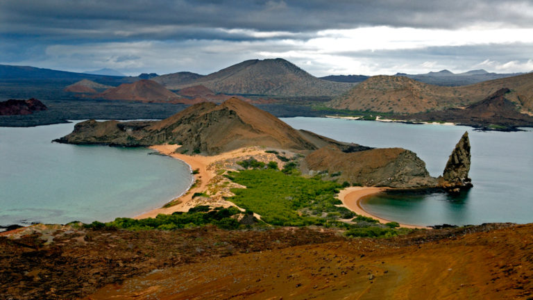 an aerial view of galapagos bay with rocks jutting out of water, green hillsides, and empty pristine beaches