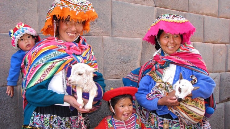 two women in colorful local clothing with two goats and two children in peru