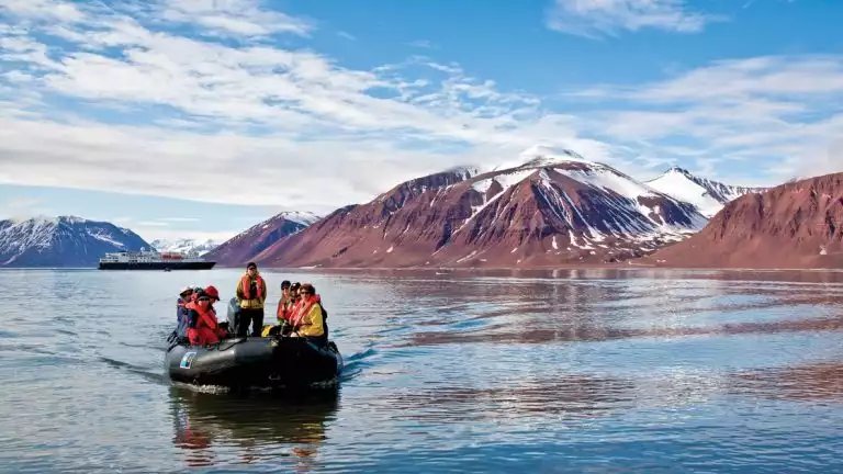 Arctic travelers on a Zodiac cruise during a sunny day with brown hillsides in the background.
