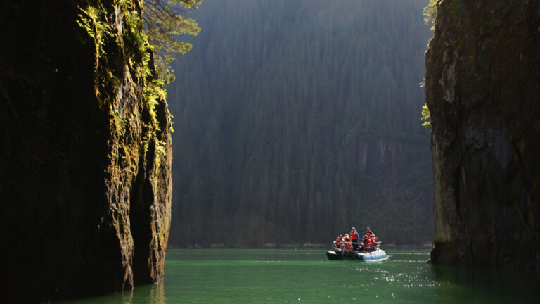 Zodic explring the narrow waterways of Alaska shown between 2 large landforms on a bright sunny day