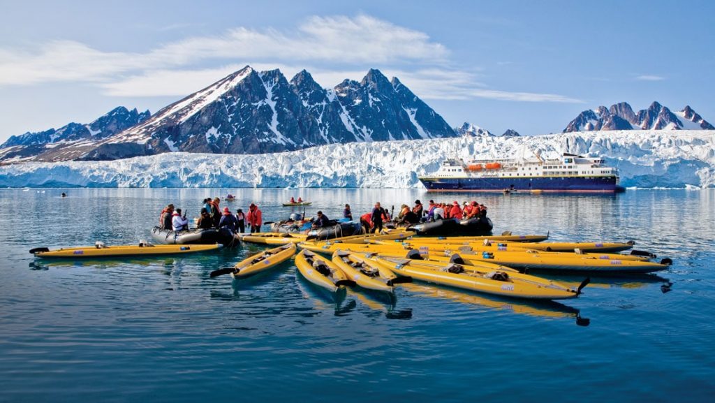 Empty yellow inflatable kayaks fan out over calm water with snowy mountains in the background during the Norway Fjords Arctic Svalbard voyage.