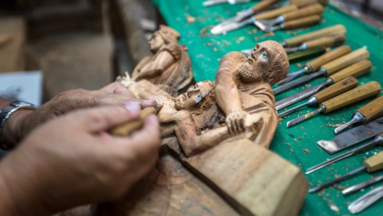 Artisan carves small wooden statues with various knives laid out on a green workbench, seen on the Otavalo Escape tour in Ecuador.