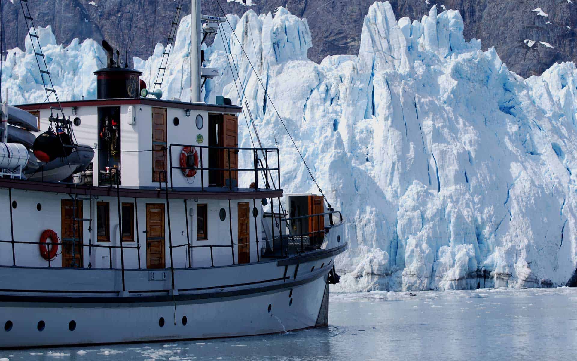 pacific catalyst alaska small ship anchored on a calm day in front of a large glacier