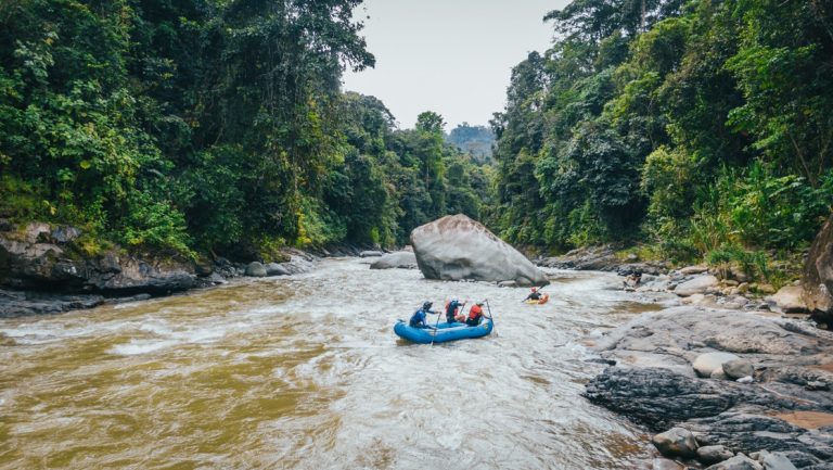 Travelers paddle a large blue raft down a whitewater river with lush jungle on both sides during the Pacific Costa Rica tour.
