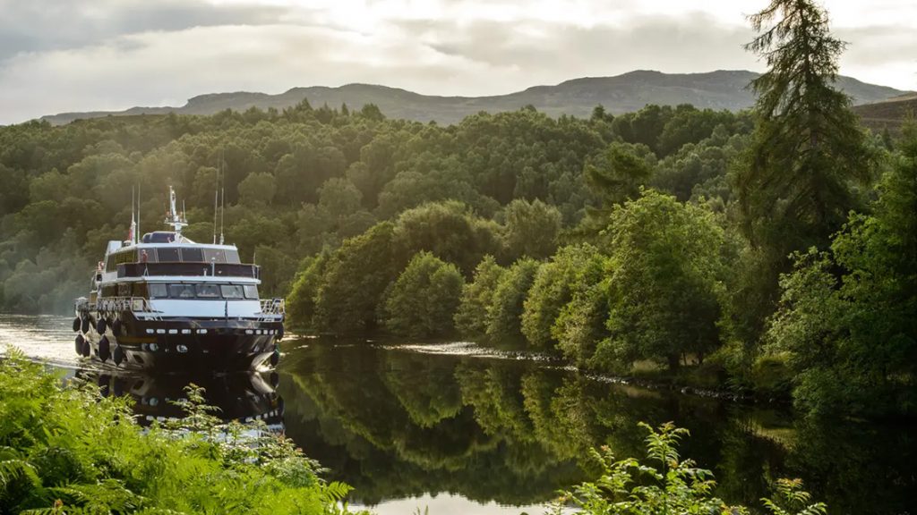 A small cruise ship naviagating through the lush green landscape