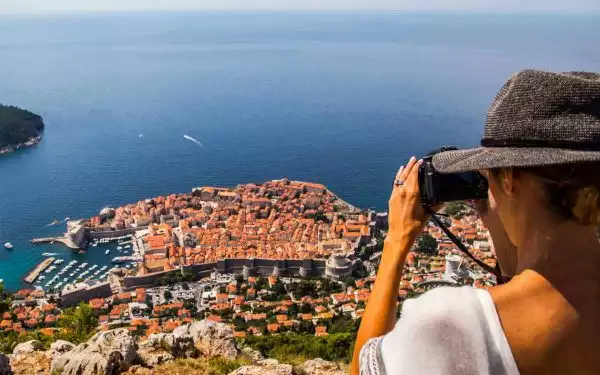 Mediterranean cruise photographer reviews a scene overlooking Dubrovnik with the red roofs and walled city surrounded by the Adriatic Sea.