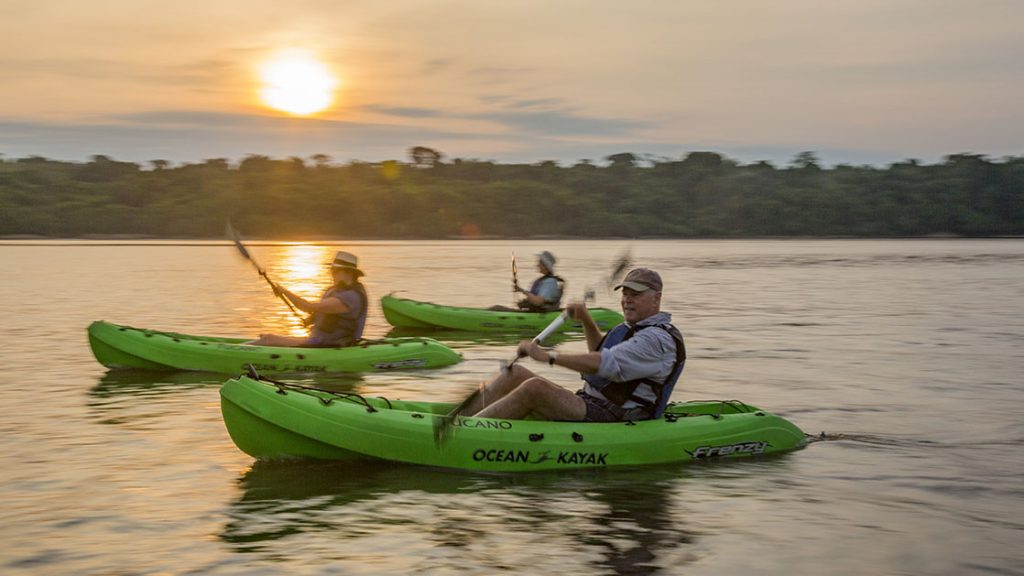 Three kayakers in green kayaks paddle at sunset in the Amazon in Brazil