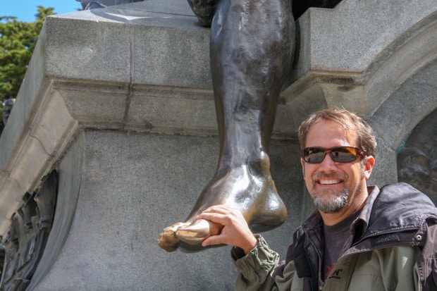 AdventureSmith Founder Todd Smith touching the Ferdinand Magellan Memorial statue's toe for good luck in Punta Arenas. 