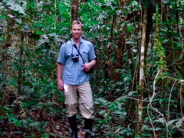 A man with binoculars and rain boots standing in the Ecuadorian Amazon jungle. 