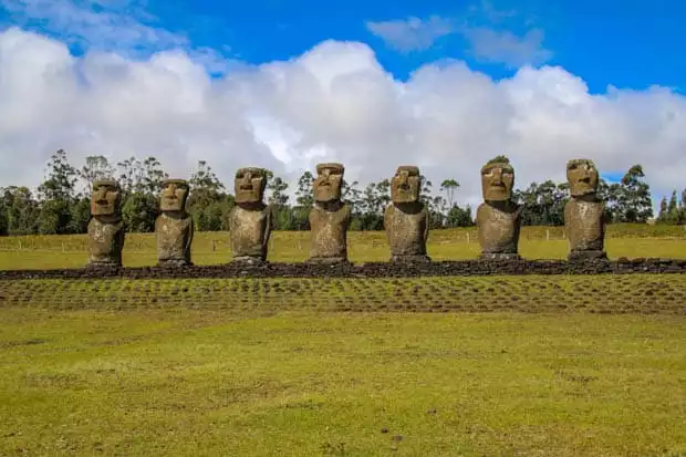Moai statues lined up with green grass and big clouds.