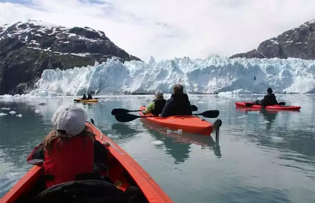 group of alaska small ship cruise travelers kayaking in front of a glacier on a sunny day