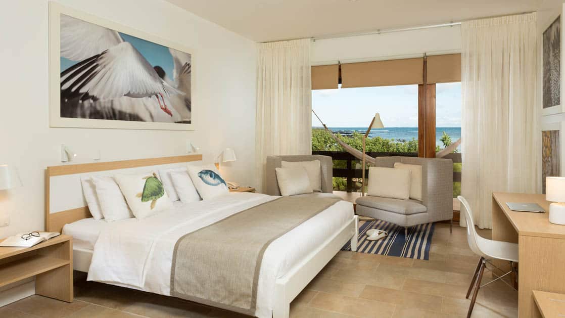 Finch Bay Eco Hotel room with large bed, large windows with ocean view and chairs.