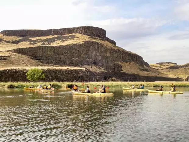 Guests from a small ship river cruise kayaking on the Palouse River near cliffs. 