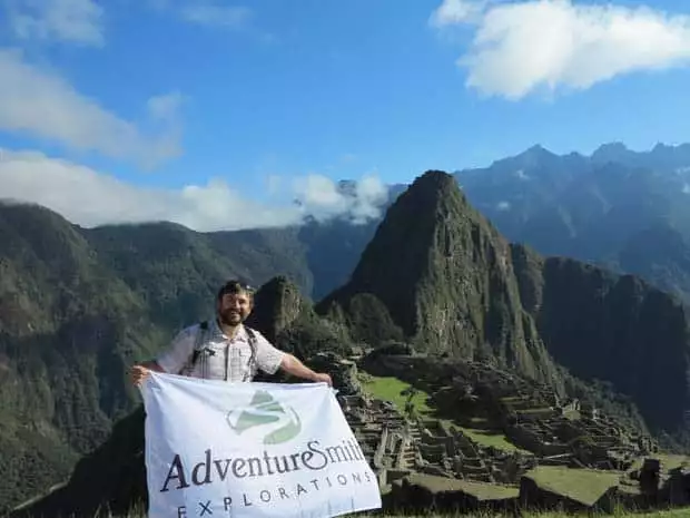 Single traveler holding a Adventuresmith Explorations flag in front of Machu Pichu.