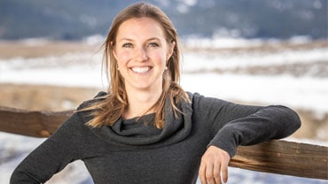 adventuresmith explorations specialist lauren pilholski leaning against a fence smiling with snow in the background