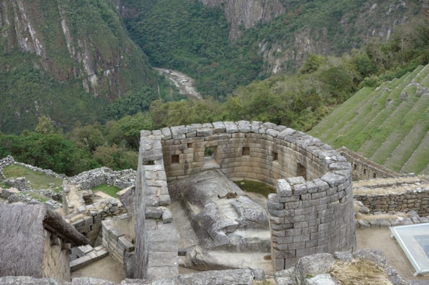 Stone building in the Machu Picchu ruin with terraced grassy areas and forest.