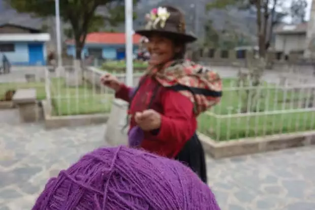 Purple yarn and a traditionally dressed Peruvian woman in a courtyard in a village.
