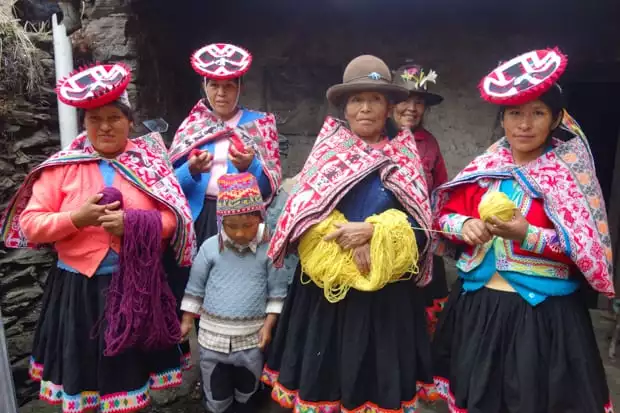 Peruvian ladies wearing hats and dressed in colorful traditional dress holding purple and yellow yarn.