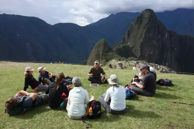 Group of travelers and guide sitting and snacking with Machu Picchu in the background.