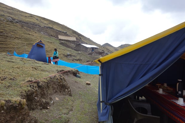 Blue tent with a long dining table with colorful textiles on a mountain hillside with a local mom and child dressed in colorful traditional Peruvian clothing.