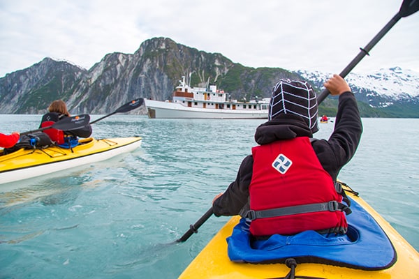 child kayaking in front of a small ship in Alaska on a family trip