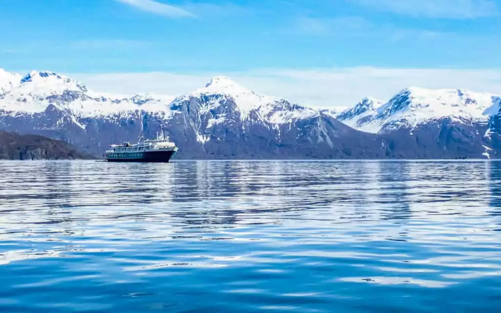 Wilderness Adventurer small ship sailing in Alaska in calm waters with snow mountains behind.