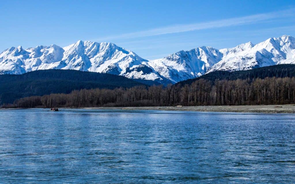 A raft floating down the Alaska river the Chilkat with the snowy Chilkat Mountain Range behind.