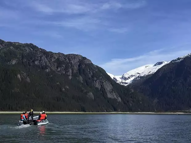 Alaska travelers in a skiff heading towards a beach under steep mountains in Alaska.