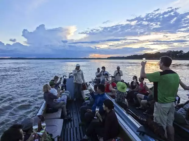 A group of people on a motorized canoe enjoying a champagne toast while the sun sets. 