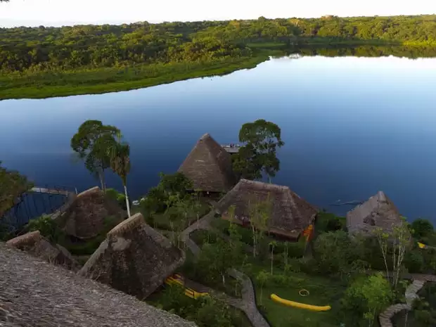 View of Napo from above of thatched roof huts and gardens with the river and jungle in the background.