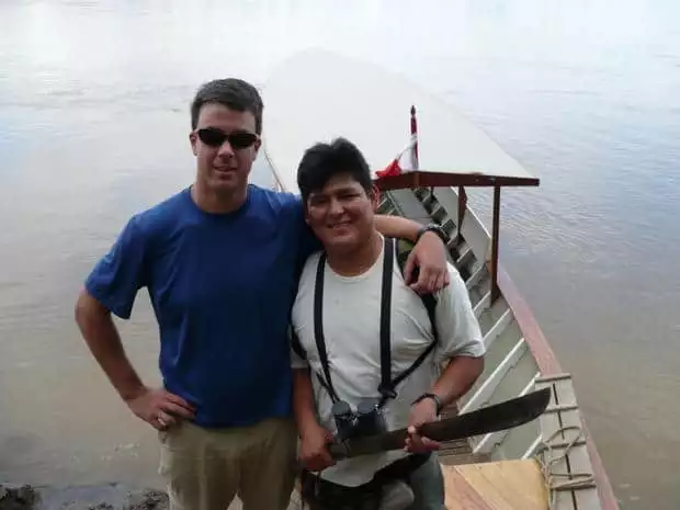 a traveler and guide holding a machete in front of a small open air boat.