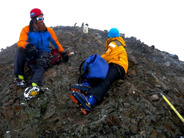 Guests taking a break on their mountaineering excursion next to penguins in Antarctica. 