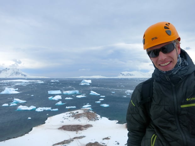 Happy guest from a small ship expedition smiling with icebergs in the background. 