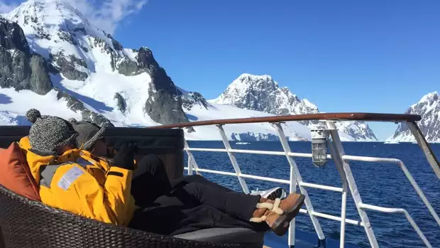Guests lounging in the sun on a sofa bed outside on deck of their small ship cruise in Antarctica. 