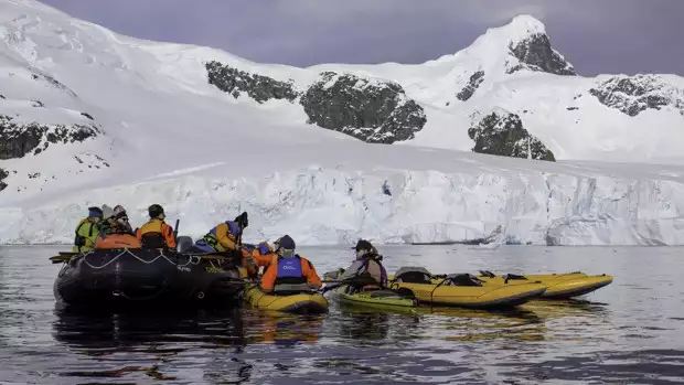 Small ship cruise guests entering kayaks from skiff in Antarctic. 