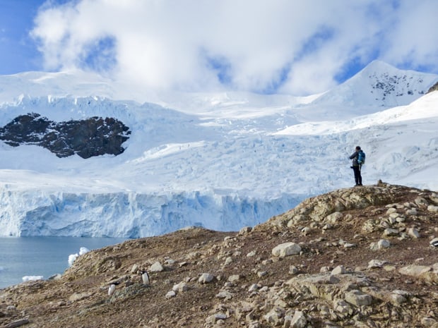 Man standing on rocks looking at the snowy landscape of Antarctica. 