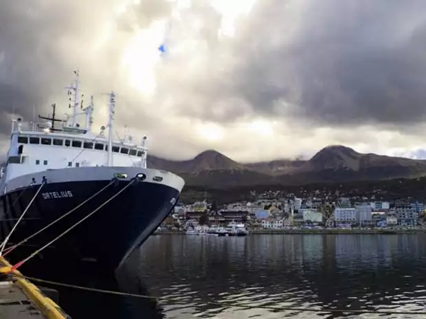 Ortelius ship anchored in Ushuaia with the city and mountains in the background.