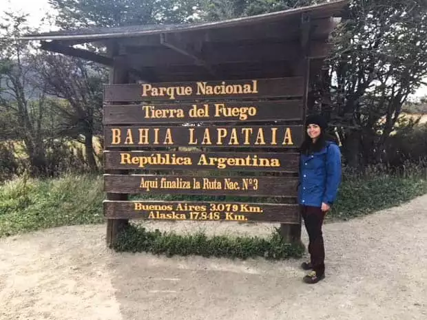 Person smiling in front of the Tierra del Fuego National Park entrance sign in Ushuaia Argentina. 