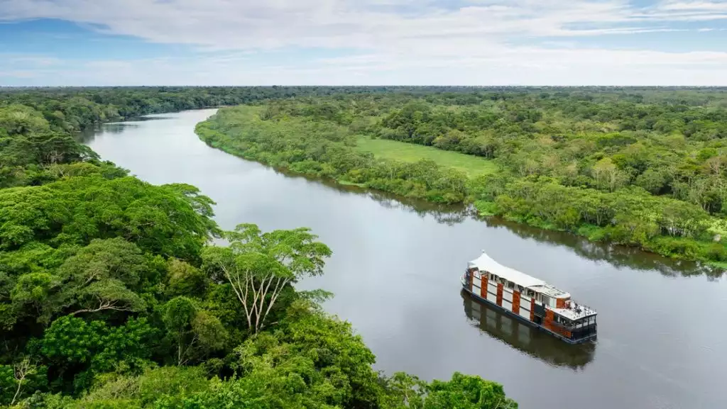 The luxury riverboat Aria Amazon navigates a winding river through the lush green jungle of the Peruvian Amazon.