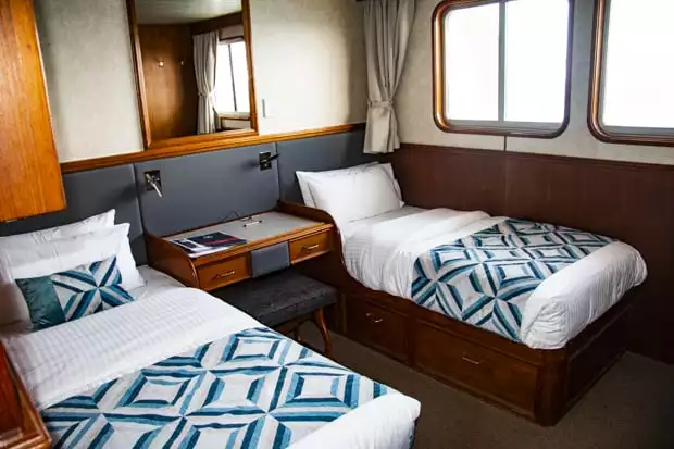 A cabin in the Coral Expeditions II with two twin beds, little desk and windows.