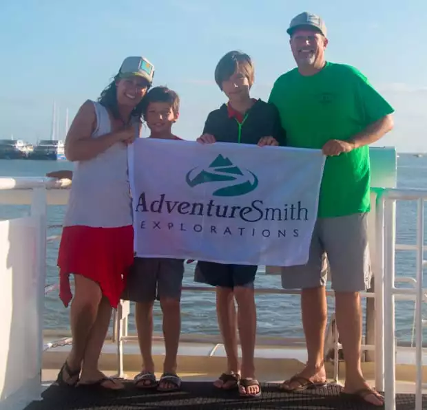 Todd and his family holding an AdventureSmith Explorations flag on the dock after a Great Barrier Reef small ship cruise.