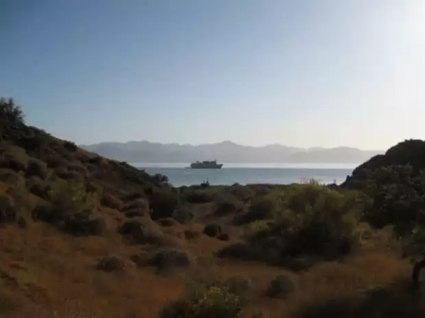 Dry desert grasslands with a small cruise ship in Baja with mountains in the background.